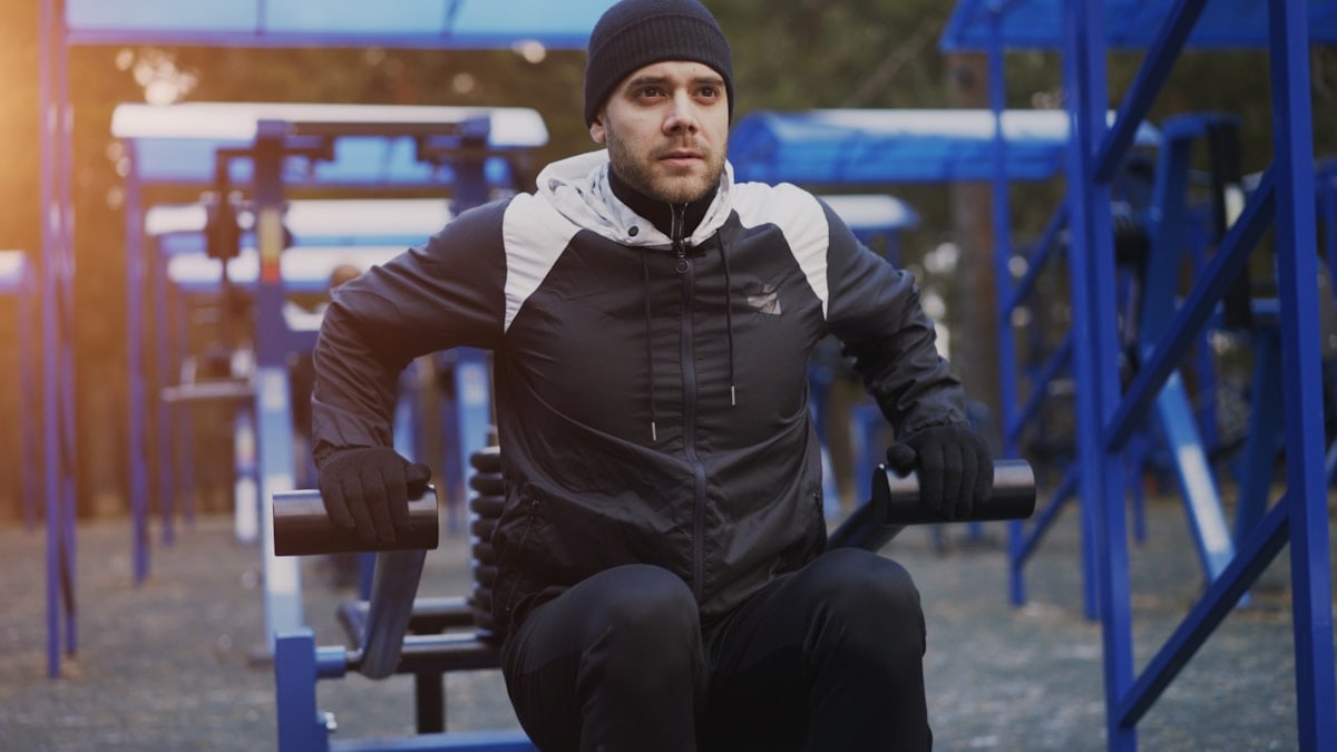 Attractive young man doing exercise in outdoor gym in winter park